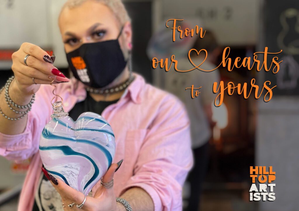 Photo of a Hilltop Artist holding up a blown glass heart "From our hearts to yours."