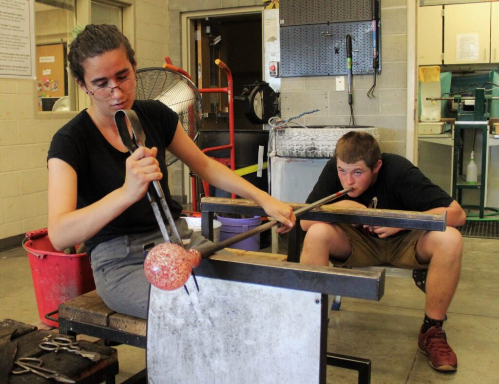 Visiting Artist Lea is assisted by Hilltop Artist Tanner in the hot shop