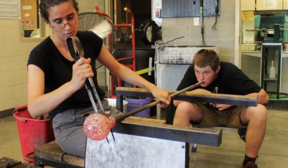 Visiting Artist Lea is assisted by Hilltop Artist Tanner in the hot shop