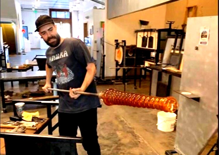 Photo of Dylan Atinkson-Betz working on a glass piece in the hot shop