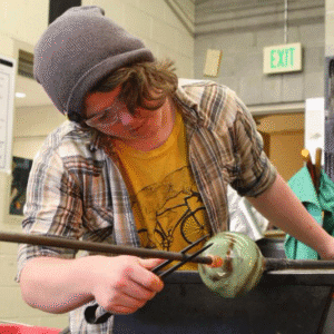 Hilltop Artist Asa working on a glass piece on the bench in the hot shop