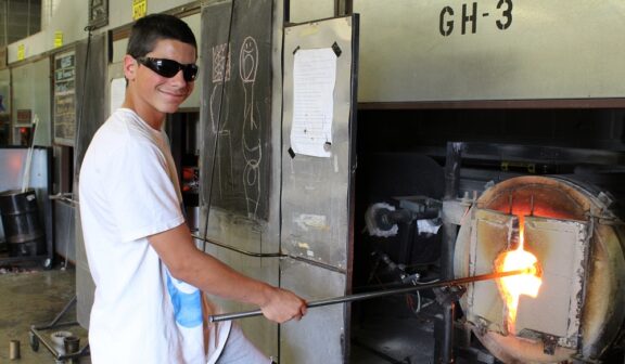 Hilltop Artist Ari heats a glass piece in the furnace at Hilltop Heritage MS
