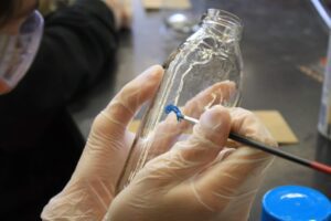Image of Hilltop Artists student painting on a glass bottle.
