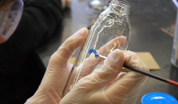 Image of Hilltop Artists student painting on a glass bottle.
