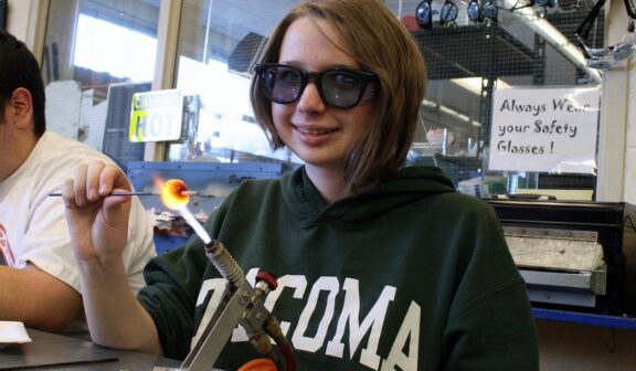 Hilltop Artist Emily works on a bead on the torch in the hot shop.