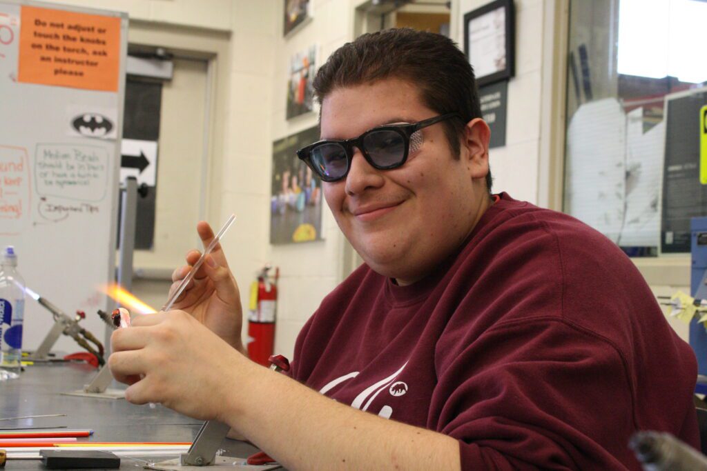Hilltop Artist student Luis working on bead torch in the hot shop.