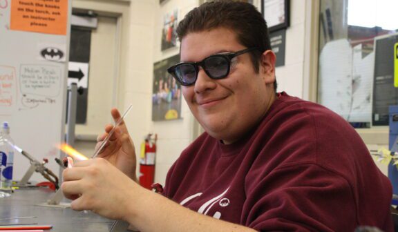 Hilltop Artist student Luis working on bead torch in the hot shop.
