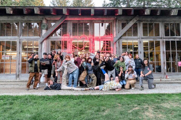 Group photo of Hilltop Artists staff and students posed under a large neon 