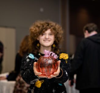 Hilltop Artists student holding out a blown glass pumpkin during the 2024 Better Futures Luncheon
