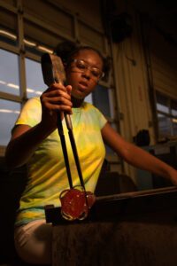 Hilltop Artist student works on a glass piece on the bench in the hot shop