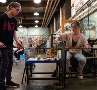 Photograph of two Hilltop Artists students collaborating on a piece in the hot shop at Silas High School