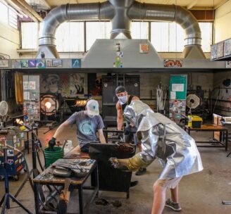 Photograph of Hilltop Artists instructor and students working on a piece in the hot shop