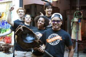 Hilltop Artists Instructor Trenton poses with students in the hot shop