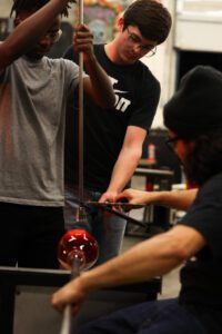 Hilltop Artists Instructor Trenton works with Production students in the hot shop