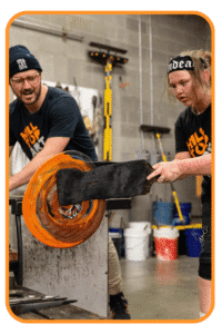 Hilltop Artists instructor, Jonathan, assists student Dasein on the glassblowing bench