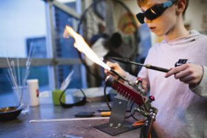 A student works on the flameworking torch in the hot shop at Hilltop Artists