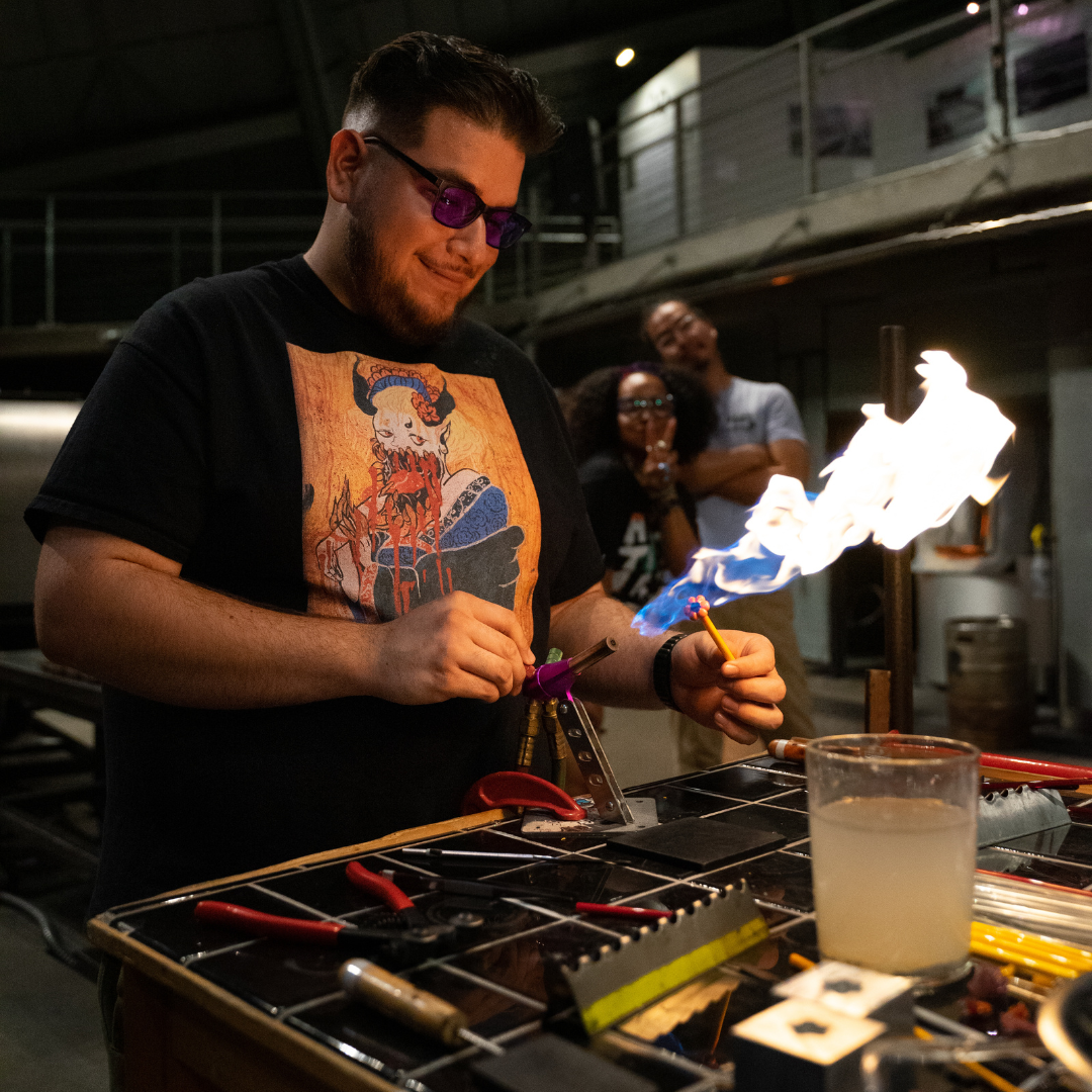 Photograph of Hilltop Artists Program Manager Luis Sanchez working on a flameworking torch in the Museum of Glass hot shop.