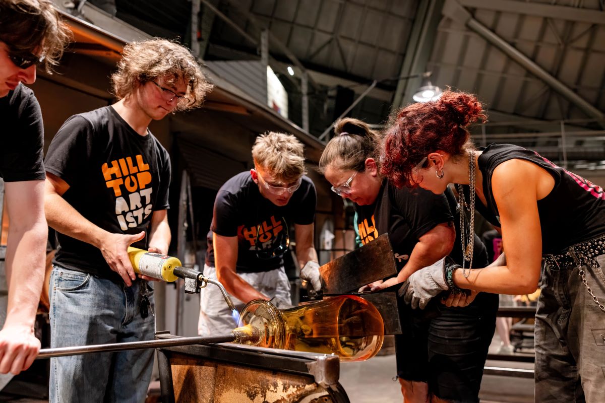 Photograph of Hilltop Artists students and Museum of Glass staff collaborating during a demonstration.