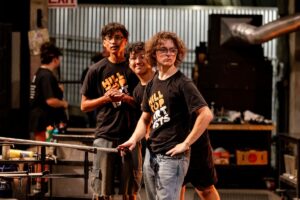 A group of students pause during a break on the hot shop floor at Museum of Glass during the annual Hilltop Artists residency.