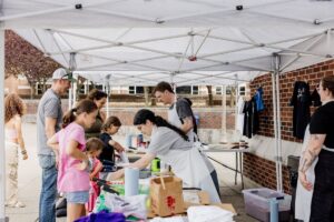 A volunteer assists community members at the screen print station during the Arts Night Out Block Party.